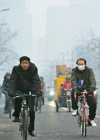 Beijing citizens ride bicycles under heavy smog