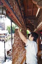 Worker hangs reed screen below eaves of Dogo Onsen spa resort landmark