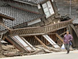 Noto earthquake - Woman walks by collapsed houses