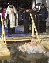 Orthodox Church priest prays as follower soaks in icy water