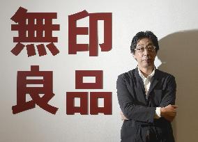 Ryohin Keikaku president poses by "Muji" brand logo