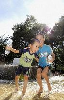 Children play around water fountain under summer sun