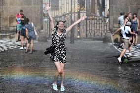 tank truck sprinkles by water the Hradcany Square in front of the Prague Castle, woman, rainbow