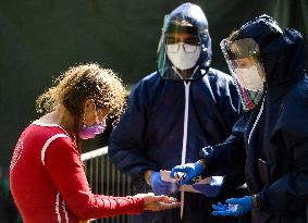 medics disinfect hands of a woman during waiting to take a sample for a covid-19 test