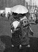 Two Japanese women walk holding a parasol.
