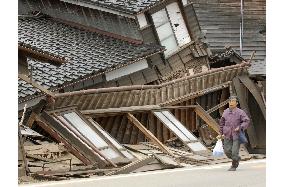 Noto earthquake - Woman walks by collapsed houses