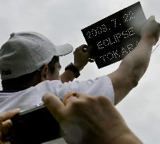 Man holds perforated board as eclipse obscured by cloud