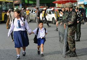 Thai schoolchildren walk past soldiers standing guard