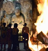 Visitors watch stone Buddhas lit by bonfire