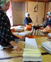 Women in traditional costume make rice sticks