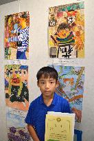 Grade school boy poses before award-winning drawing