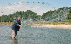 Man casts fishing net to catch salmon in Fukushima river