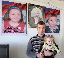 Syrian man holds sister in front of photos of kin killed in war