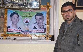 Palestinian man stands by photos of kin killed in war