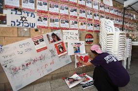 An Israeli woman hangs a placard on a wall covered with  photographs of some of those taken hostage by Hamas