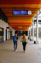 Travelers Beneath The Timetable At A Germann Train Station